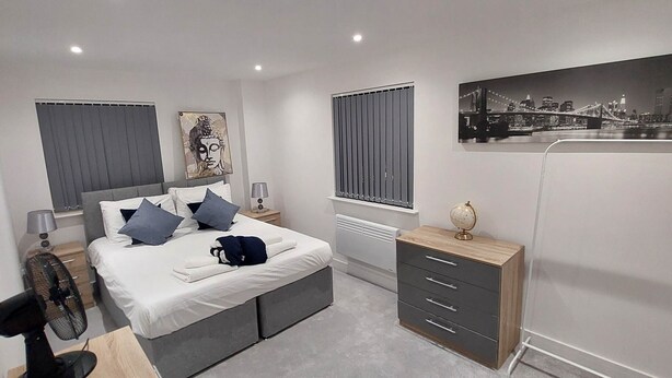A modern bedroom with a bed, bedside tables, a nightstand, a fan, a dresser, and artwork on the walls.