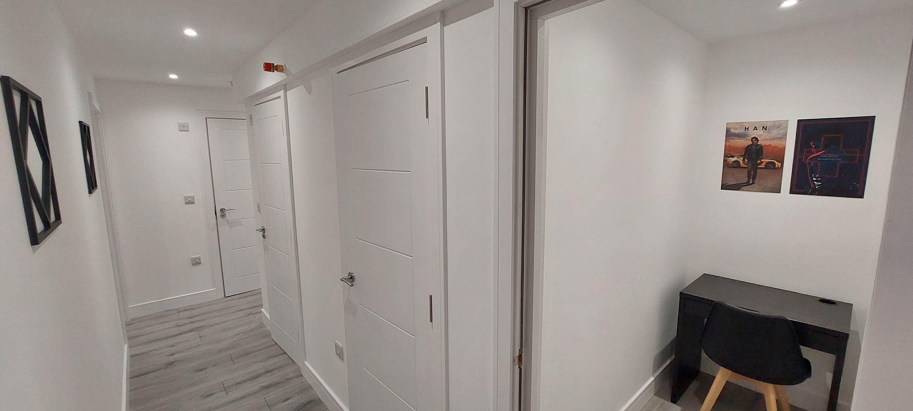 Un couloir avec des portes blanches, un bureau avec une chaise et deux tableaux encadrés accrochés au mur.