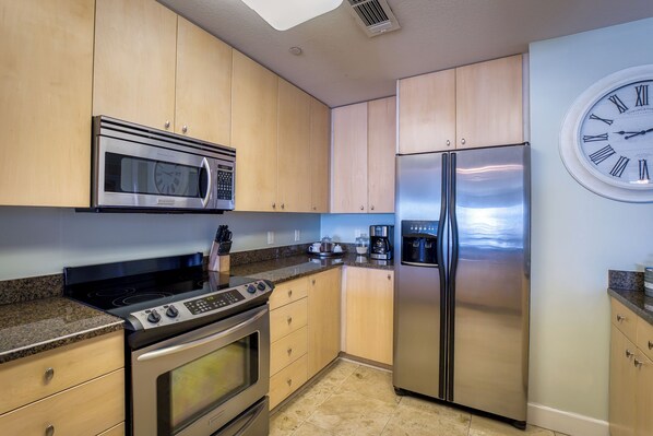 A kitchen with wooden cabinets, stainless steel appliances including a microwave, stove, and refrigerator, and a wall clock.