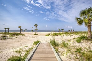A wooden pathway leading to a beach with palm trees and a clear sky.
