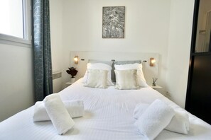 A hotel room with a large bed, two bedside lamps, a wall-mounted artwork, and a window with curtains.
