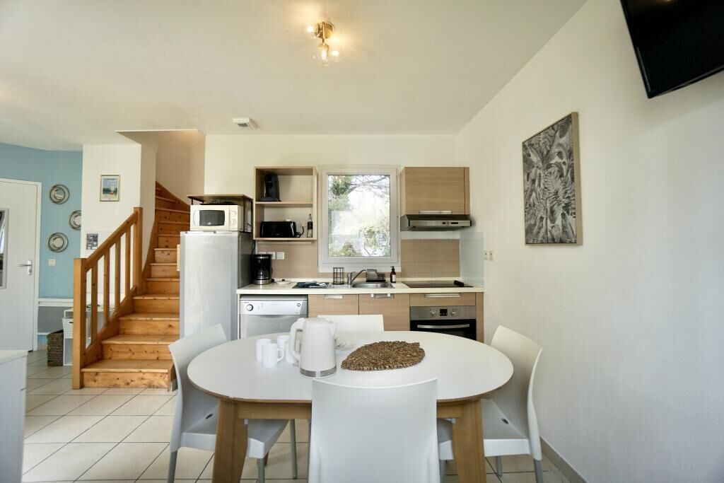 A modern kitchen with a dining area, wooden staircase, and a flat-screen TV mounted on the wall.