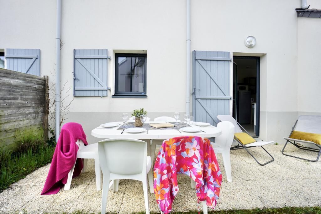 An outdoor dining area with a table set for two, white chairs, and a covered tablecloth.
