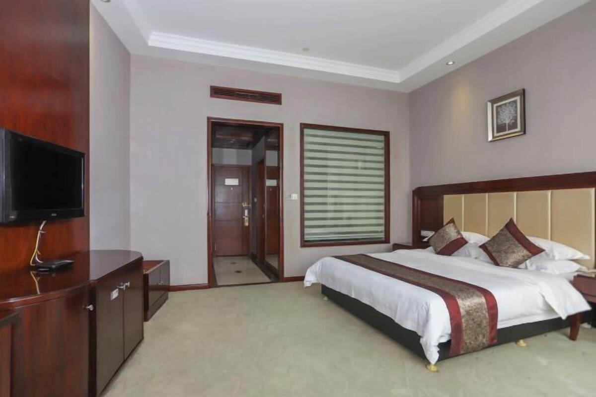 A hotel room with a bed, a television, a wardrobe, and a door leading to a bathroom.