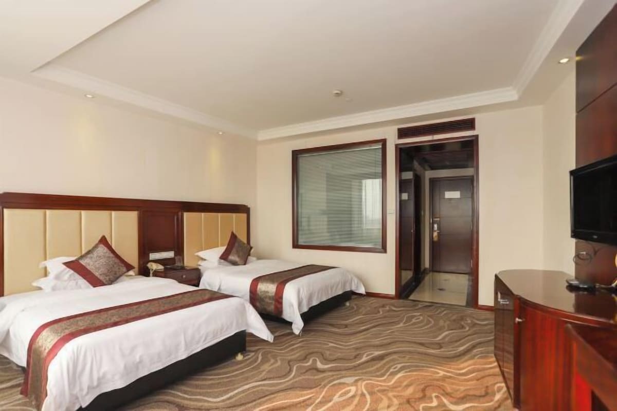 A hotel room with two beds, a television, a desk, and a large window.