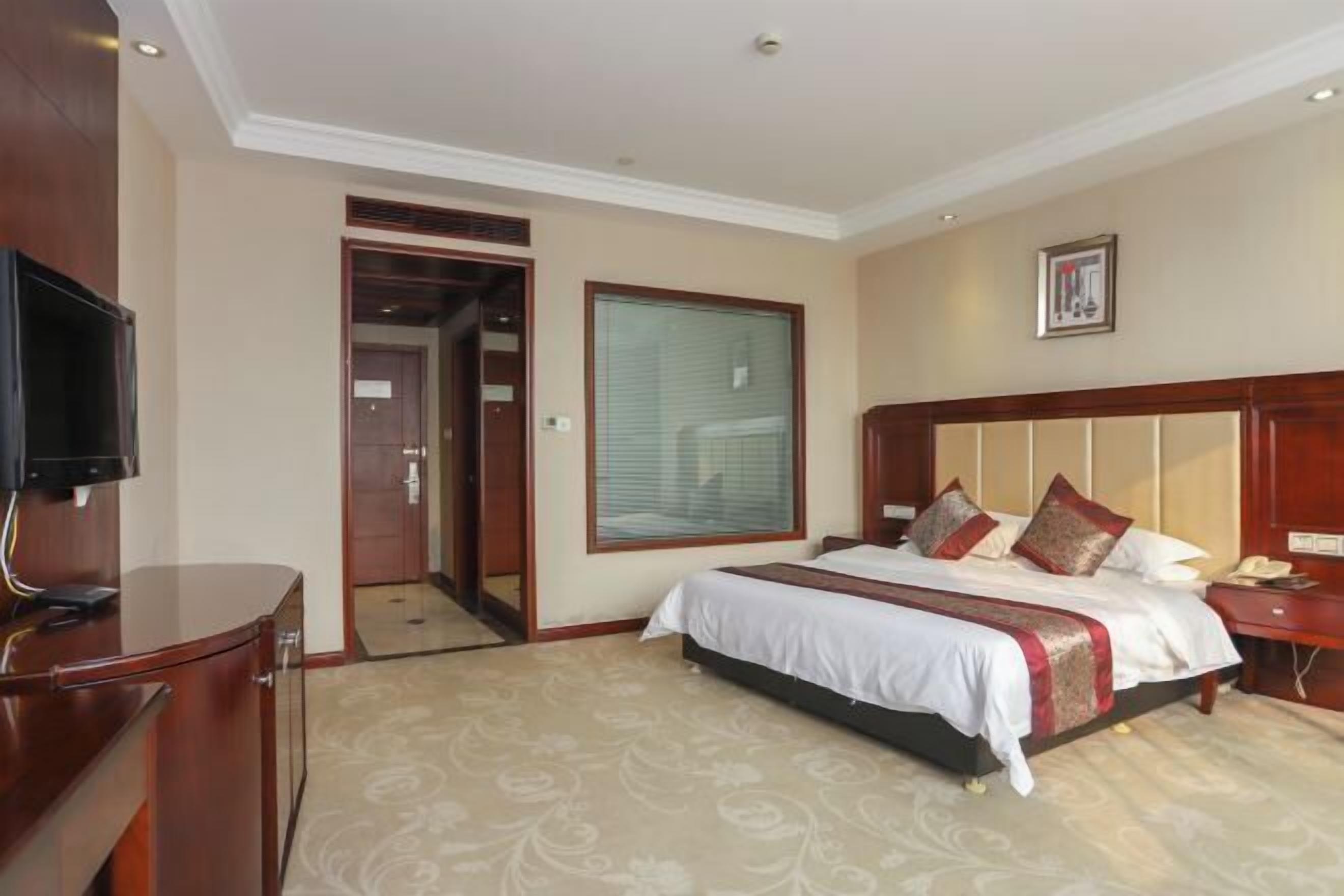 A hotel room with a bed, a television, a desk, and a door leading to another room.