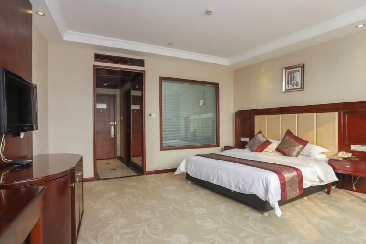 A hotel room with a bed, a television, a desk, and a door leading to another room.
