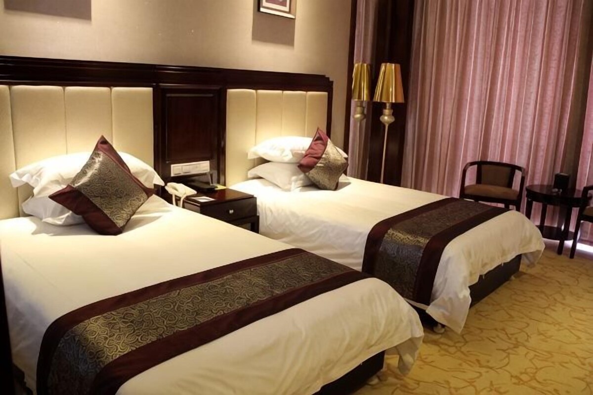A hotel room with two beds, a nightstand, a lamp, and a chair.