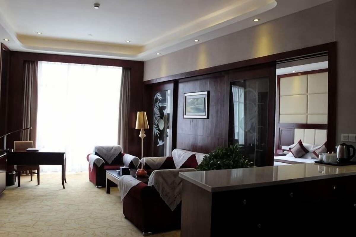A hotel room with a sofa, a desk, a chair, a coffee table, and a large window.