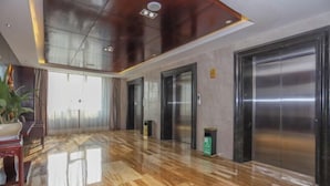 A spacious lobby with polished wooden floors, a reception desk, and three elevators. - Huatai Hotel (Tianmen)