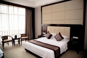 A hotel room with a large bed, two chairs, a nightstand, and a window with curtains. - Huatai Hotel (Tianmen)