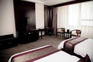 A hotel room with two beds, a desk, a television, and a seating area with chairs.