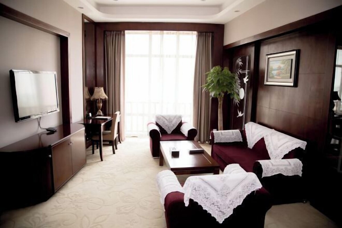 A hotel room with a TV, a desk, a chair, a sofa, and a plant.