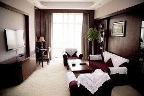 A hotel room with a TV, a desk, a chair, a sofa, and a plant. - Huatai Hotel (Tianmen)