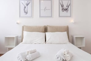 A neatly made bed with white linens, two pillows, and rolled towels on the bed. There are three framed pictures on the wall above the bed. - 2-Bedroom Apartment in Milan (Milano)