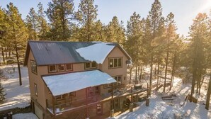 Une maison à deux étages, avec un toit enneigé et un balcon, entourée d’arbres.