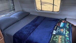 Ein kompaktes Wohnmobil-Interieur mit Bett, Fenster und einem kleinen Tisch.