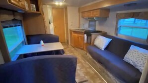 Ein kompaktes Wohnmobil-Interieur mit einer Küchenzeile, einer Essecke und einer Sitzgruppe.