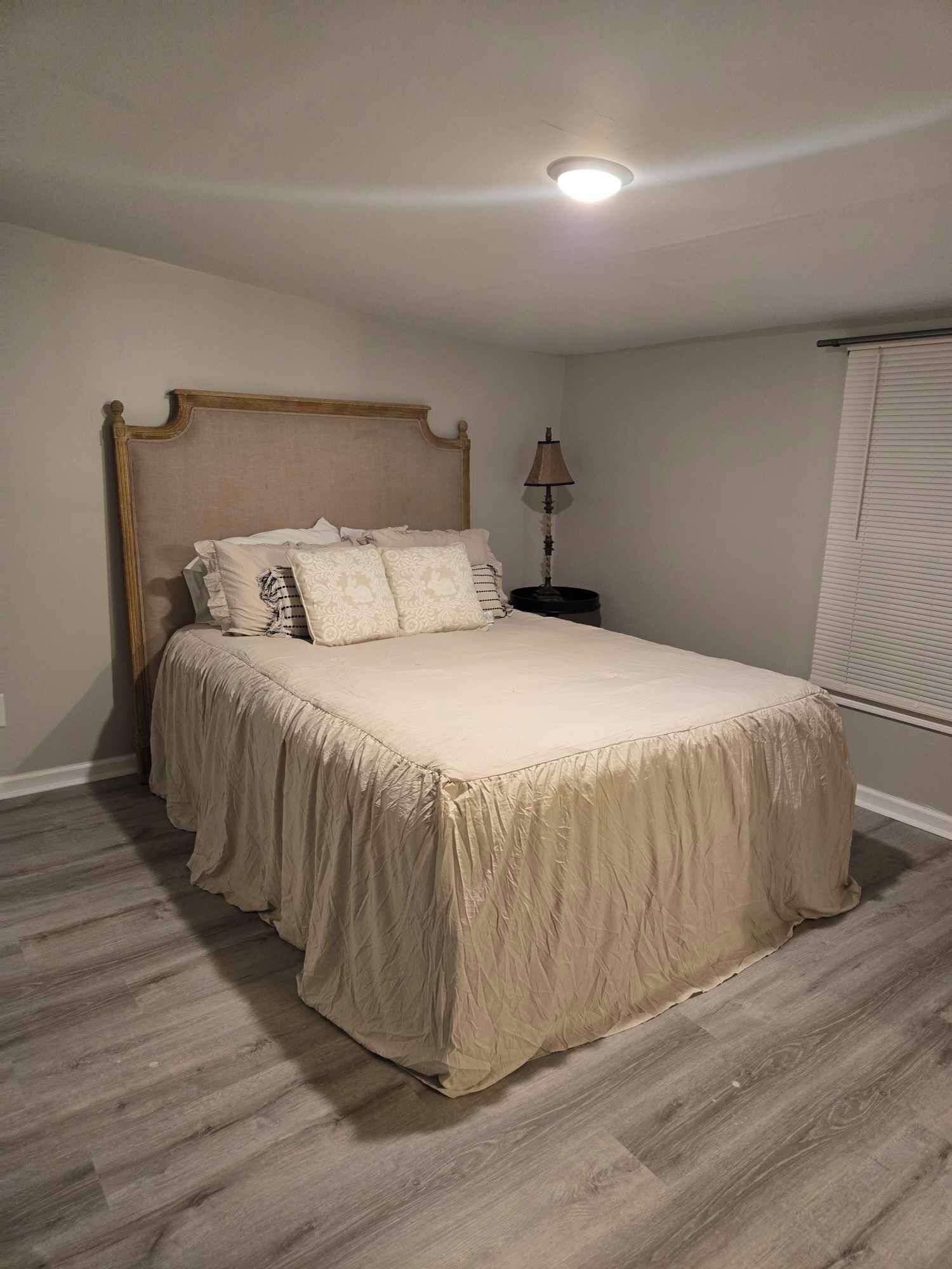 A bedroom with a bed, a nightstand, a lamp, and a window with blinds.