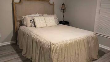 A bedroom with a bed, a nightstand, a lamp, and a window with blinds.