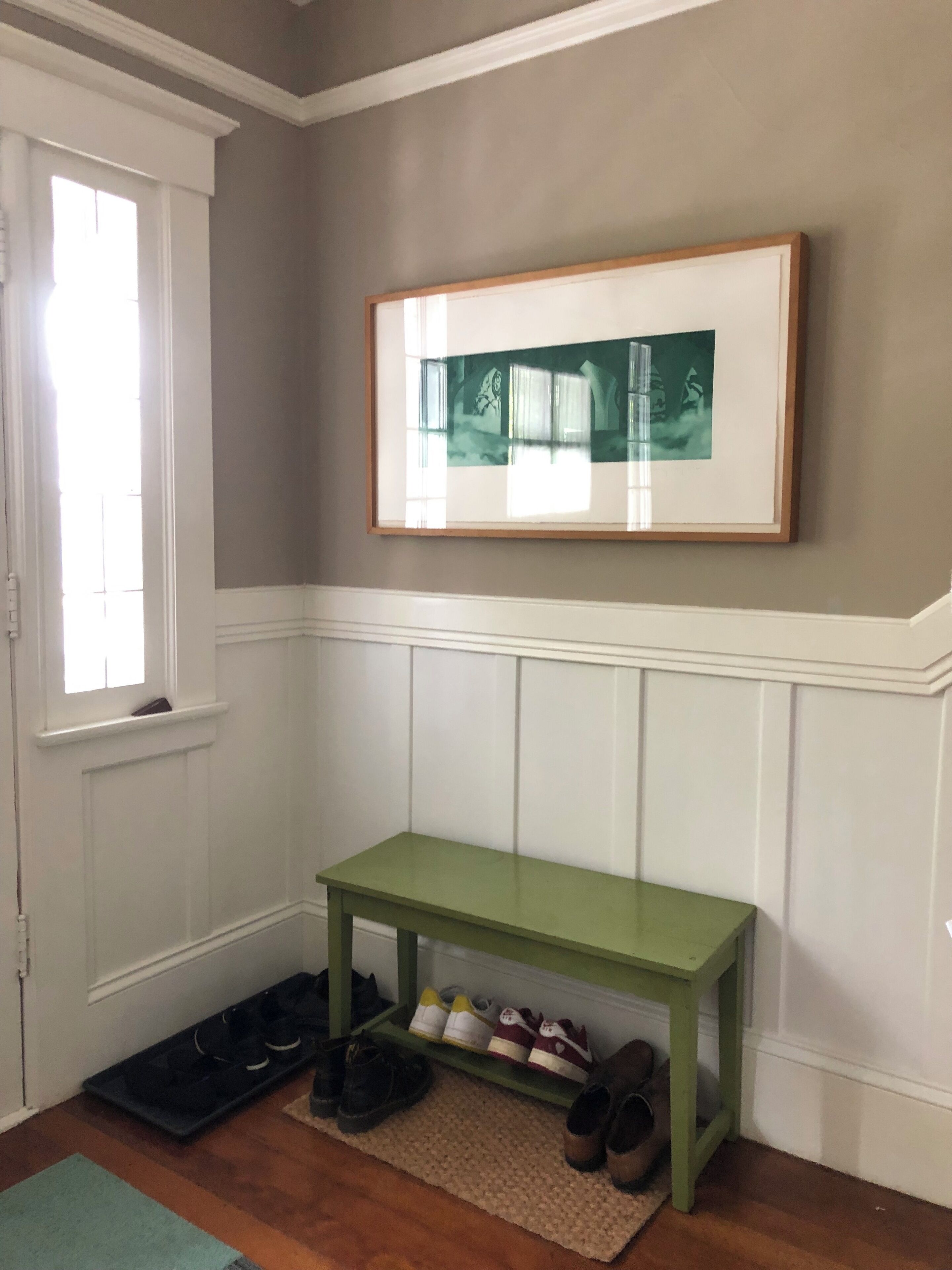 Una habitación con un banco verde, un cuadro en la pared y un zapatero con varios zapatos.