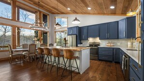 A modern kitchen with wooden floors, dark blue cabinets, and a central island with bar stools. - Enchanted Ridge Retreat: Family friendly, peaceful property, hot tub, sleeps 10 (Ellijay)