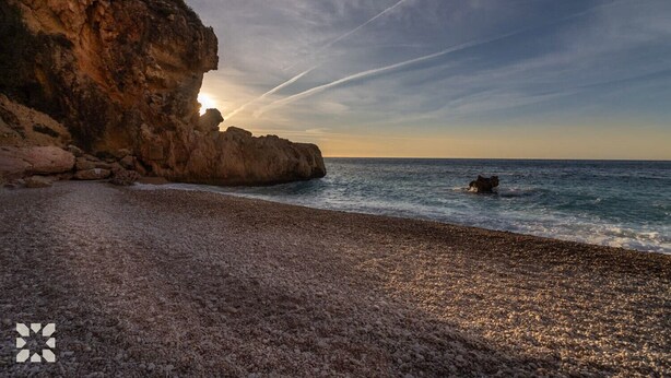 Une plage rocheuse, avec une grande falaise et des vagues déferlantes sur l’océan.