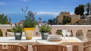 Une terrasse avec une table dressée pour le repas, des plantes en pot et une vue sur la mer et les bâtiments.