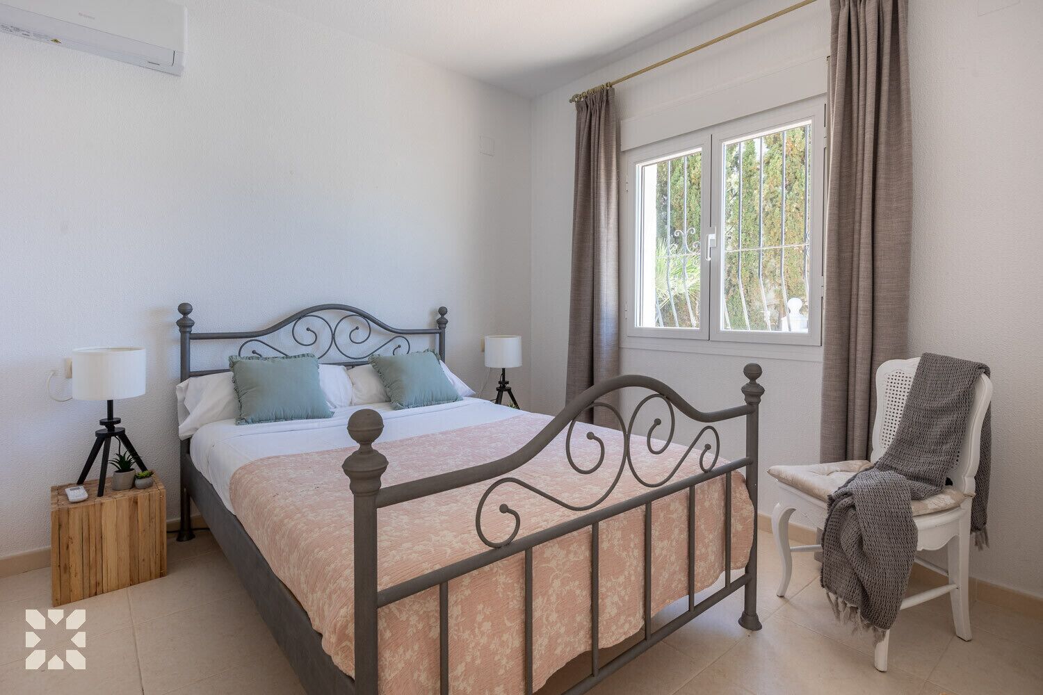 A bedroom with a bed, bedside lamps, a chair, a window, and a small table with a lamp.