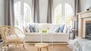 Un salon chaleureux avec un canapé blanc, un fauteuil en osier, une petite table en bois et une cheminée.