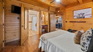 A wooden cabin interior with a bed, a ceiling fan, a mounted TV, and a dining area.