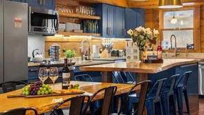 A modern kitchen with wooden cabinets, a central island with bar stools, a wine bottle, and a fruit platter.