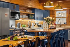 A modern kitchen with wooden cabinets, a central island with bar stools, a wine bottle, and a fruit platter. - Sleeps 20 Indoor Pool  Hot Tub  Fall Foliage  Wheelchair Access  Hocking Hills (McArthur)