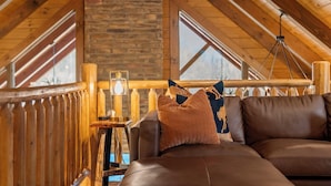 A cozy room with a stone wall, wooden ceiling beams, a leather sofa, and a hanging light fixture.