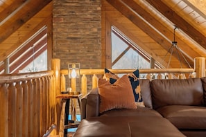 A cozy room with a stone wall, wooden ceiling beams, a leather sofa, and a hanging light fixture.