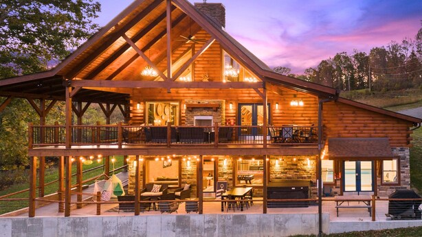 A large log cabin with a spacious deck, multiple seating areas, and a pool.