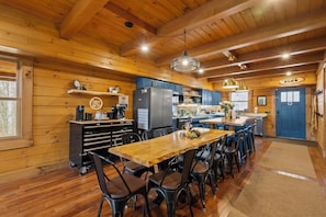 A wooden cabin interior with a dining area, kitchen, and a blue door. - Sleeps 20 Indoor Pool  Hot Tub  Fall Foliage  Wheelchair Access  Hocking Hills (McArthur)