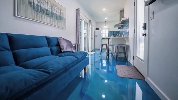 A modern living room with a blue sofa, a glass coffee table, and a large abstract painting on the wall.