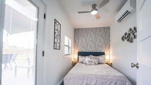 A bedroom with a bed, a ceiling fan, an air conditioner, and a window with blinds.