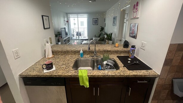 Una cocina con encimeras de granito, lavavajillas, pileta y una toalla verde colgada del mueble.