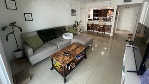 Una sala de estar moderna con un sofá gris, una mesa de centro de madera y una cocina al fondo.