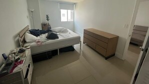 Un dormitorio con cama, cómoda, escritorio, lámpara y ventana.