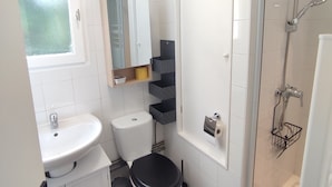 Et lille badeværelse med en hvid vask, et sort toilet, en brusekabine i glas og en hvid toiletpapirsholder.