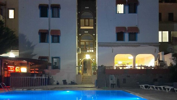 A swimming pool with a reflection of the building's windows and a well-lit entrance. - BODRUM LOTUS LINE HOTEL (Bodrum)