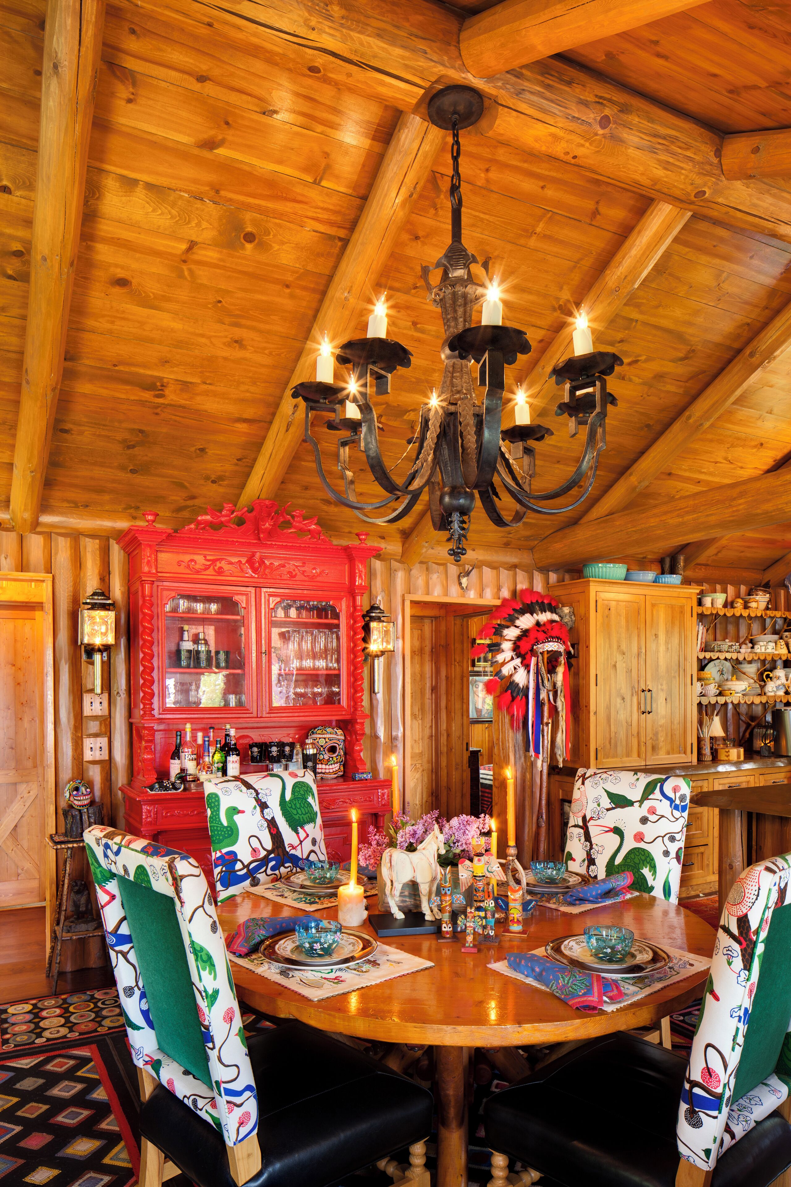 A wooden dining room with a chandelier, red cabinet, and patterned chairs.