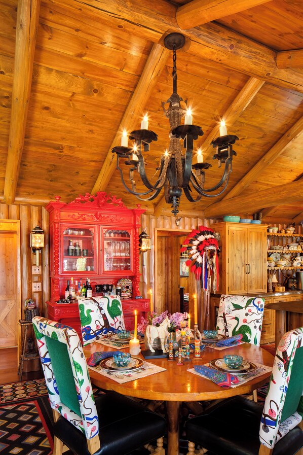 Une salle à manger en bois, ornée d’un lustre, d’un buffet rouge et de chaises à motifs.