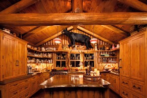 Une cuisine rustique en bois, ornée d’une sculpture d’ours au plafond, avec des armoires en bois et un grand îlot central.