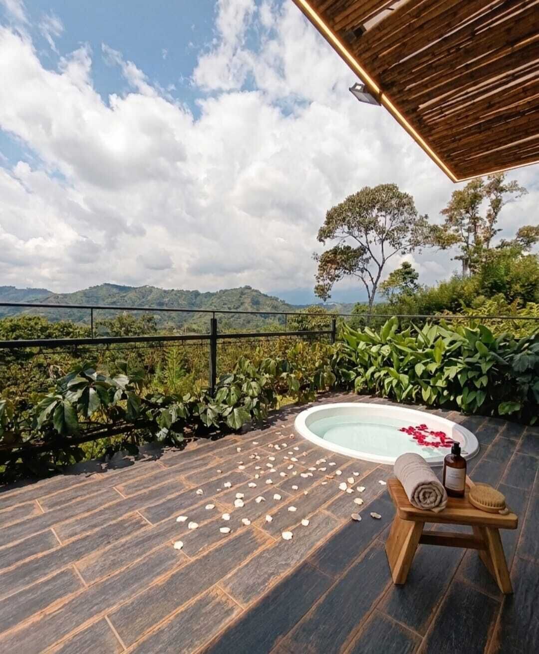 Een hottub met een houten bankje en een fles, omgeven door groen en uitzicht op bergen.