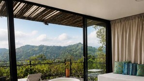 Une chambre dotée d’un grand lit, offrant une vue sur un paysage montagneux, avec un balcon et un jacuzzi, ainsi qu’un coin repas.