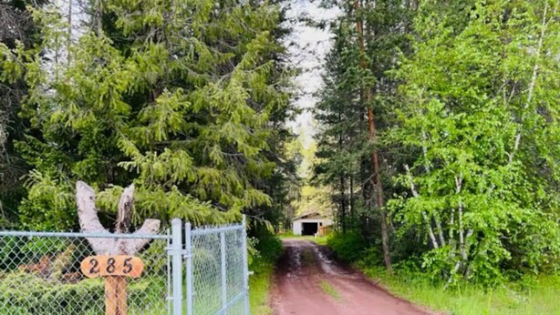 Une route de campagne avec un panneau indicateur en bois portant le numéro « 285 » et une clôture en treillis métallique.